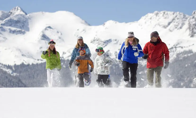 A group of seven people stomp along a snowy meadow in snowshoes